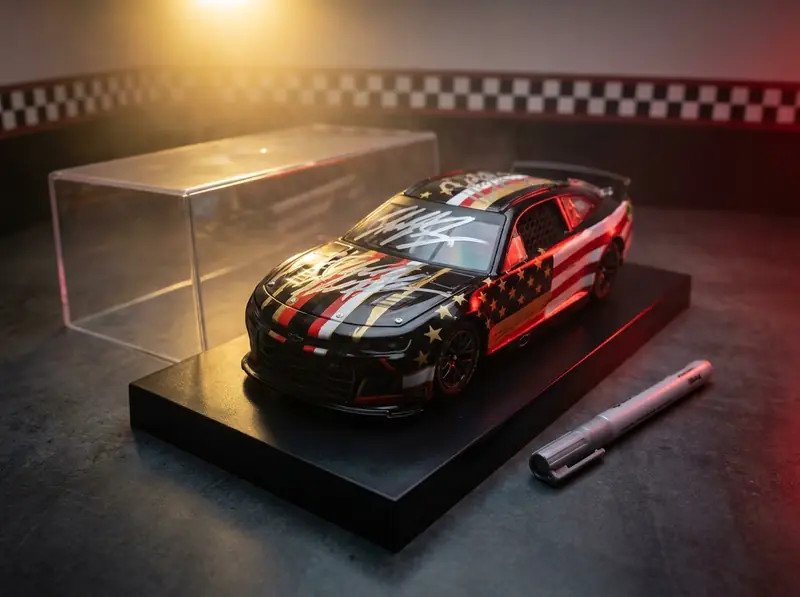 Concept illustration: a 1:24 stock car diecast in a plain black, red and gold livery on a black display base, a silver paint-marker scrawl across its hood, an acrylic cover set aside, in a race garage with a checkered wall stripe.